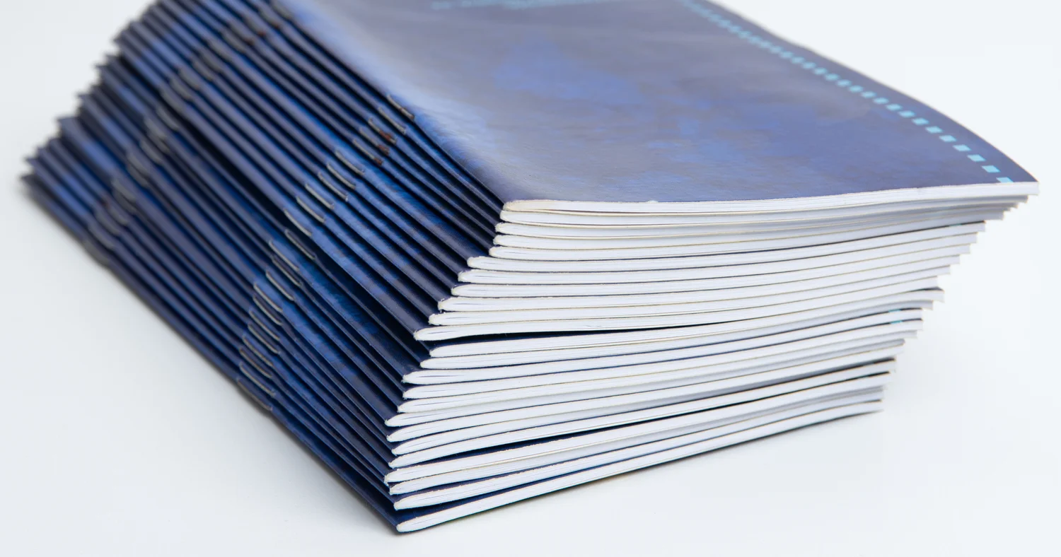 Stack of blue-covered printed brochures with white paper edges on a clean surface