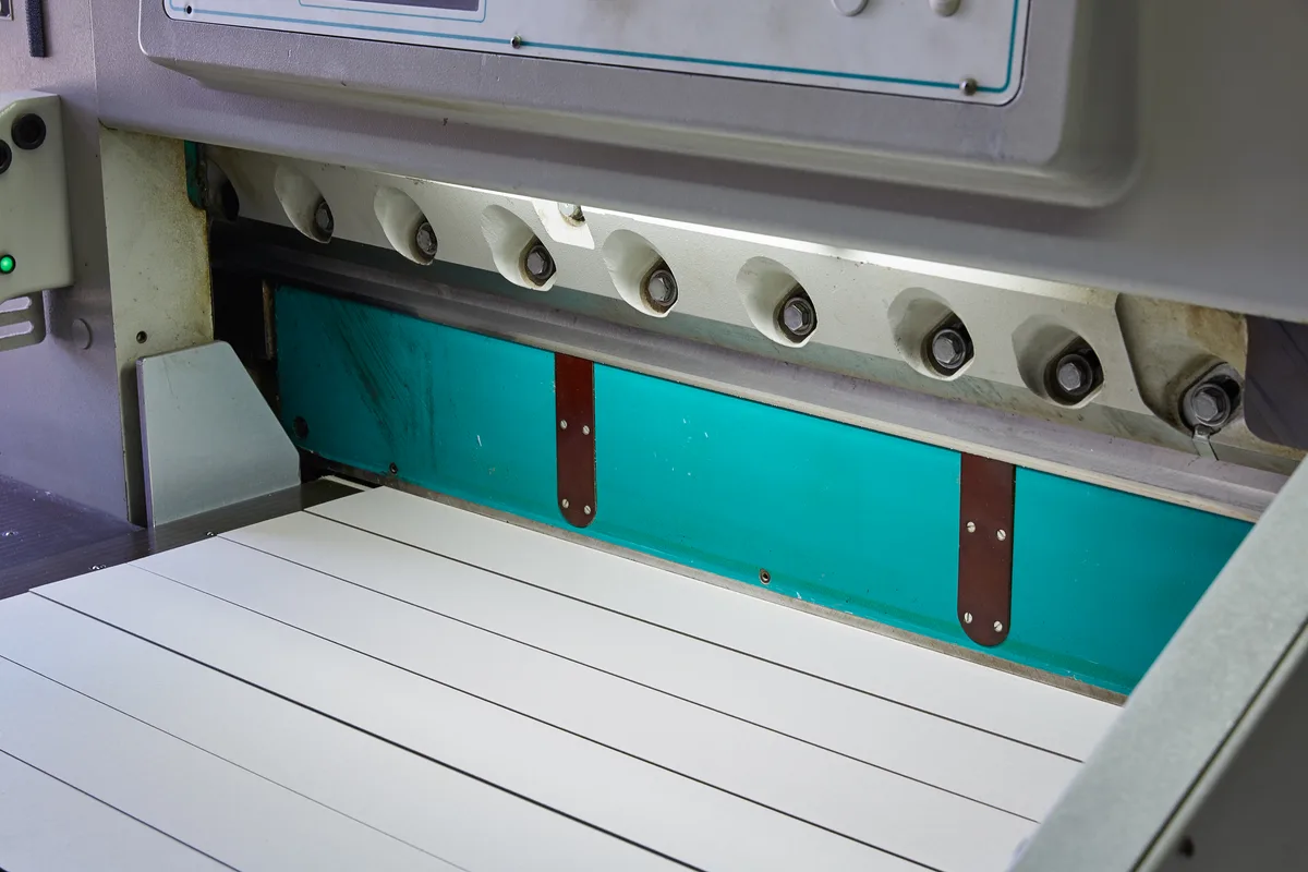 Paper sheets beneath the blade of an industrial guillotine cutter