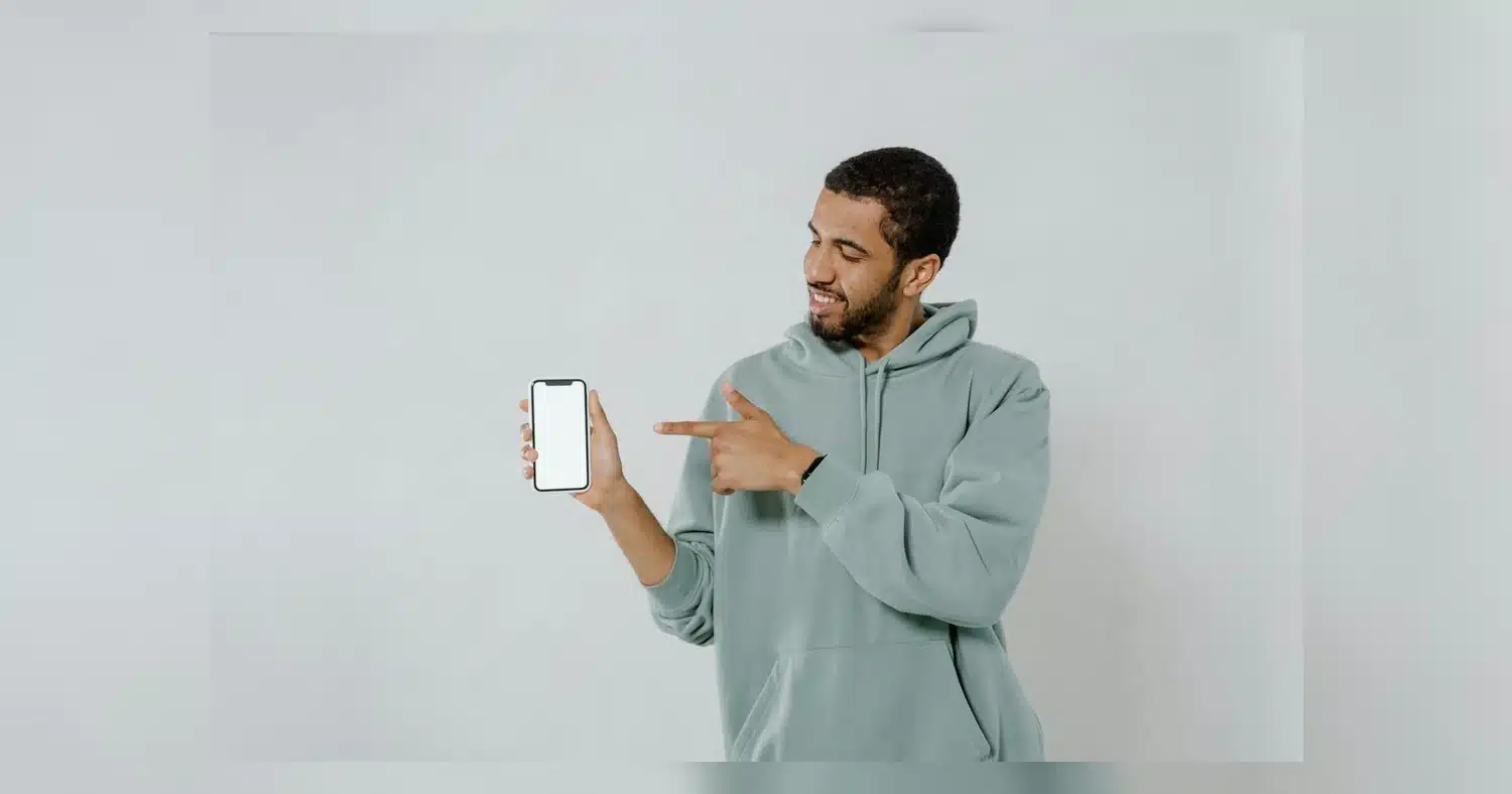 Hoodie Design Tips — Young man in hoodie points at smartphone with blank screen, offering ample copy space for designs or mes