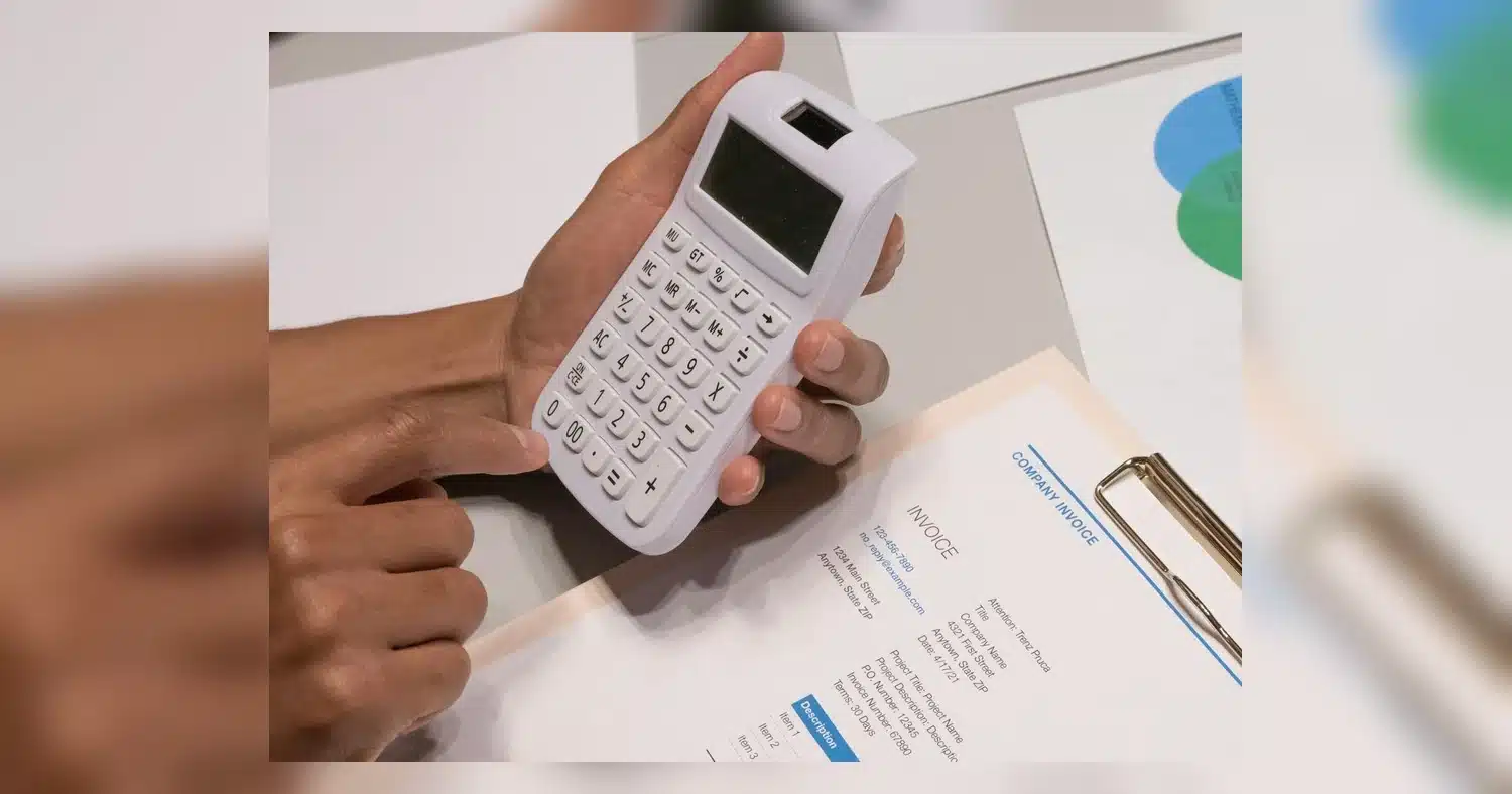 Magazine Printing Cost — Close-up of hands using a calculator next to a company invoice, depicting a financial calculation co