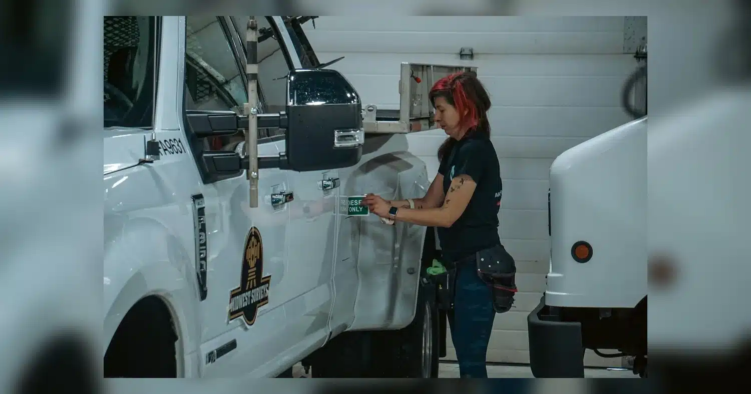 CVOR Number Decals — Woman applying a safety sticker on a truck in an indoor garage setting, Calgary, Canada.