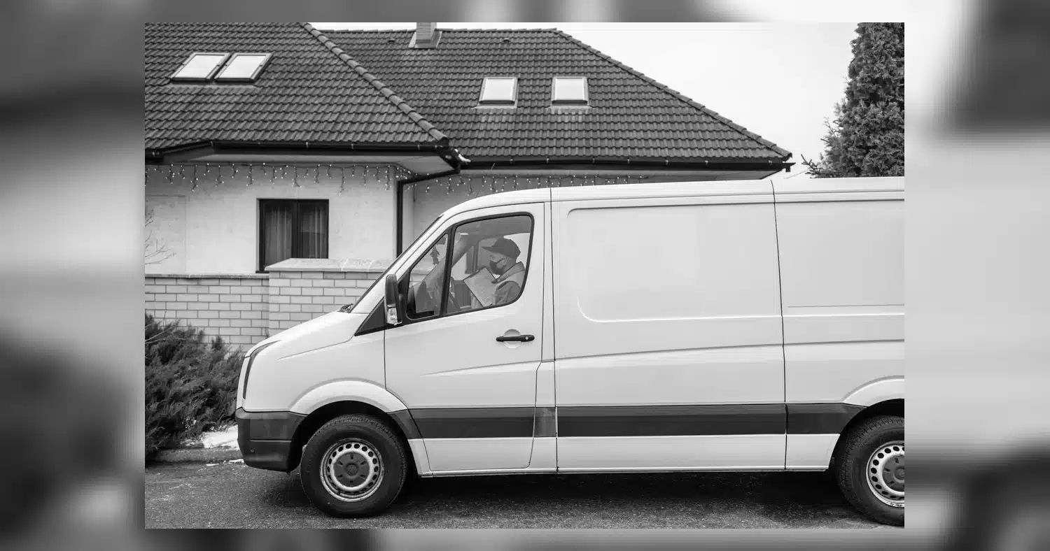 Van Decal Ideas — Side view of a white delivery van parked outside a residential house with driver reading a document.
