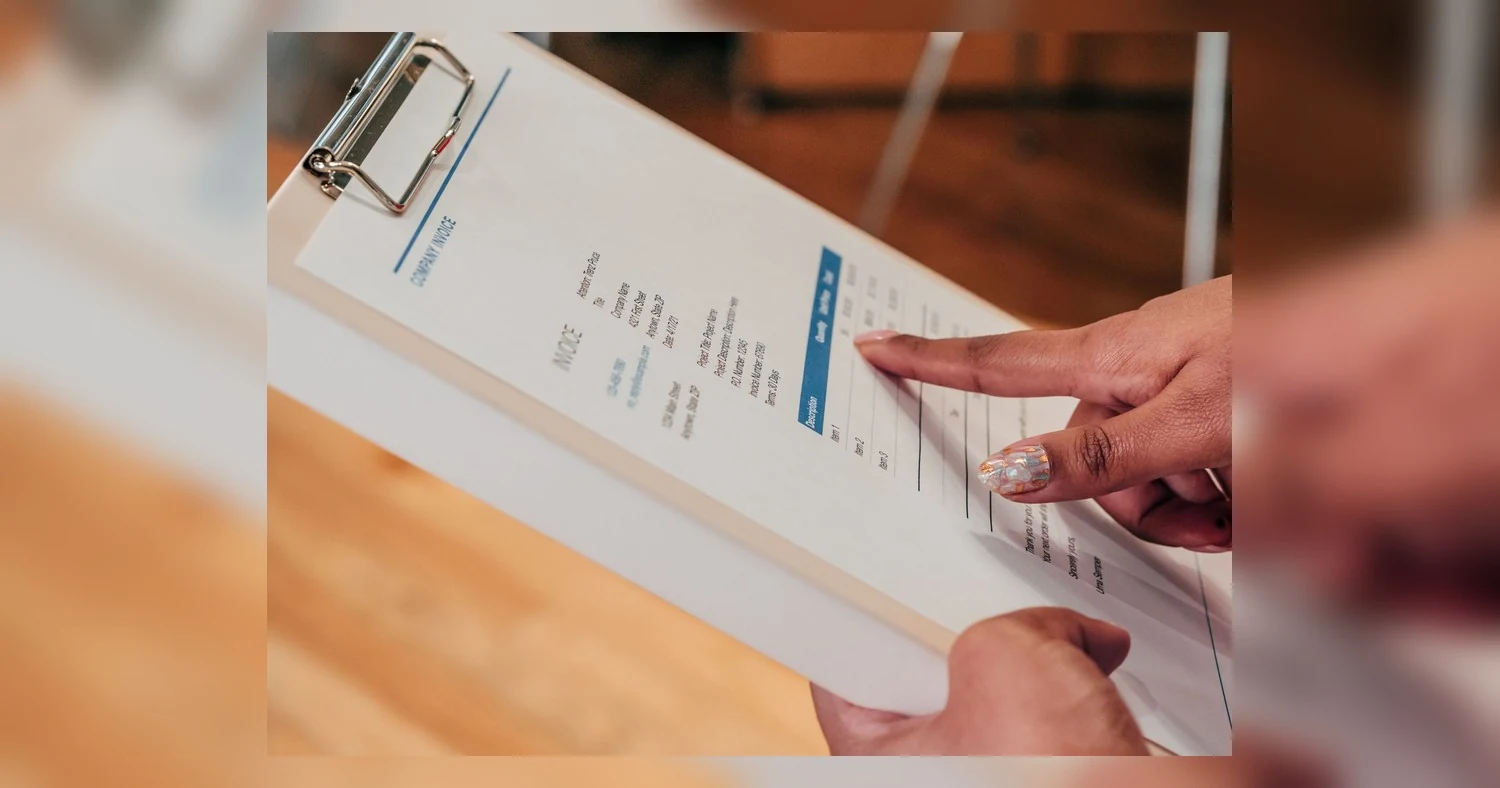 NCR forms — Close-up image of a person pointing to a document on a clipboard, indoors.