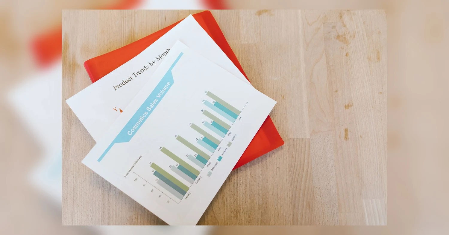 presentation folder printing — Top view of a cosmetics sales volume report with charts on a wooden desk.