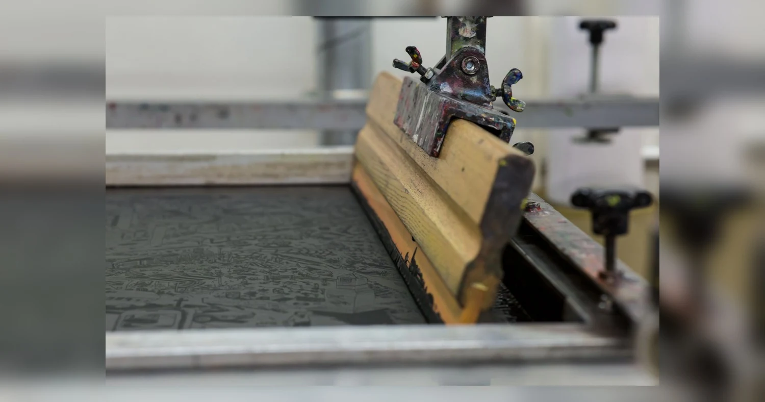 screen printing vs embroidery for custom apparel — Detailed view of a screen printing setup with a wooden squeegee in Luzern,