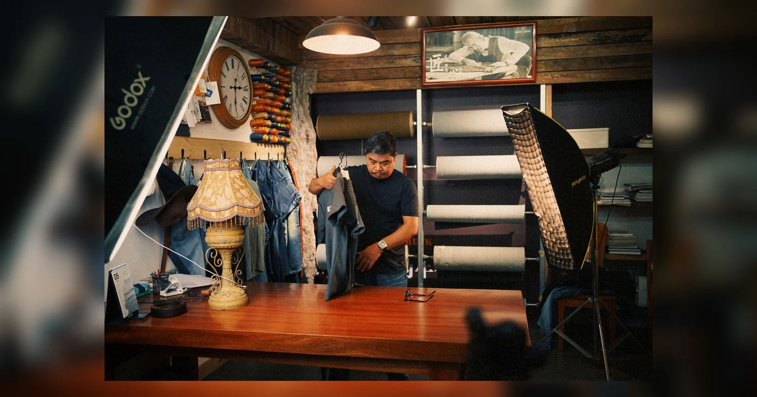 same day custom apparel near etobicoke — Male tailor in a workshop setting, arranging denim fabric under studio lighting.