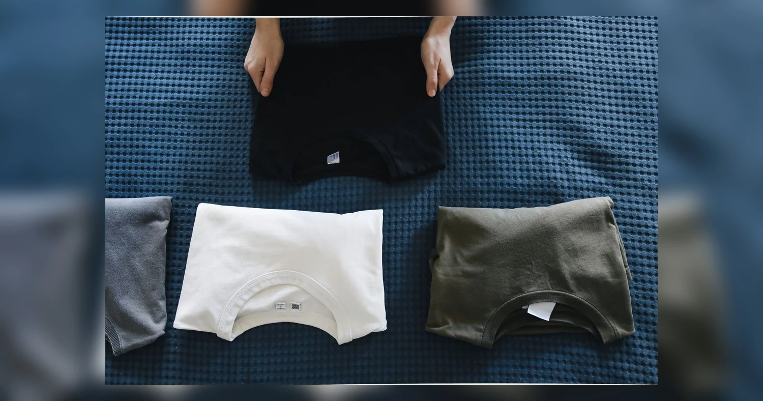 custom apparel for local promotions near etobicoke — Top view of neatly folded colored T-shirts laid out on a blue bedspread,