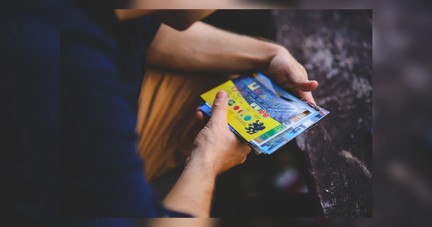 postcard printing sizes — A person holding a collection of vibrant travel postcards outdoors.